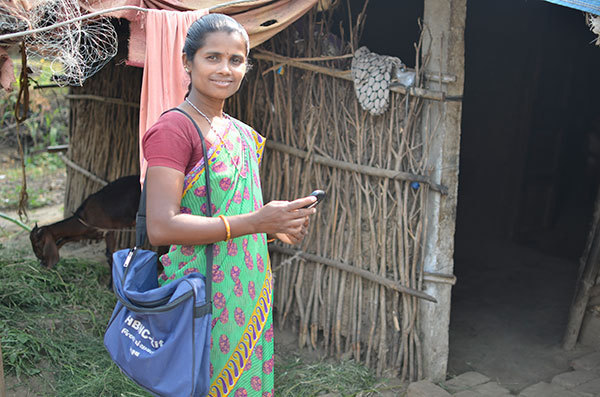 ASHA smiling and holding her smartphone as she enters the home of a patient in rural India.