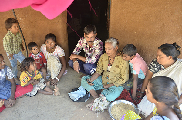 A village family in Gujarat sitting on the floor while an ASHA accesses the ImTeCHO app on a smartphone.